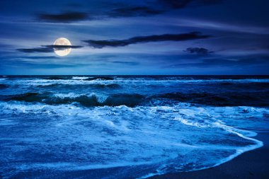 Geceleri ufuk üzerinde bulutlu gökyüzü ile dramatik deniz manzarası. Karamsar atmosferli bir tatil felaketi. Sonbaharda, dolunay ışığında sahilde doğanın güzelliği ve tehlikesi