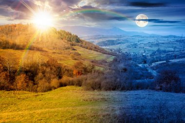 Sonbahar ekinoksunda kırsal alan. Gündüz ve gece zaman kavramını değiştirir. Yuvarlanan tepelerdeki ağaçlar. Sonbahar mevsiminde, güneşin ve ayın alacakaranlıkta olduğu dağlık kırsal manzara