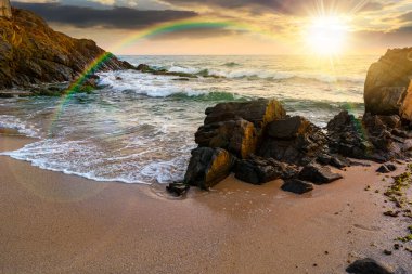 Yazın gün batımında deniz manzarası. Akşam ışığında sakin dalgalarla yıkanan kayalarla dolu güzel bir sahil. Gökkuşağının altından ufka ve bulutlu mavi gökyüzüne bak. Rahatlamak ve rahatlamak için manzaralı seyahat yeri