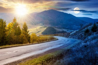 Sonbahar ekinoksunda dağ manzarası boyunca yol. Gündüz ve gece zaman kavramını değiştirir. Güneş ve ayın olduğu kırsal bir manzara. Asfalt asfalt asfalt boyunca çam ağaçları kırsal alanda geçer. seyahat arkaplanı
