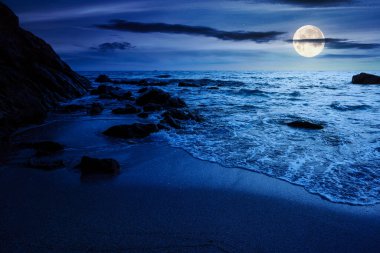 Sakin deniz manzarası. Geceleri kumlu sahilde dalgalanan kayalar. Dolunay ışığında manzaralı deniz manzarası. Rahatla ve yaz tatilinde kıyı konseptini düşün.