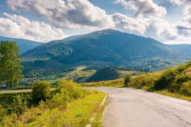 Güneşli bir akşamda dağ geçidi. Tepeden aşağı inen yol. Bulutlu gökyüzünün altında Temnatyk Tepesi 'nin önündeki Volovetler Vadisi' nin manzarası