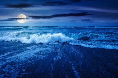 Gece fırtınadan önce deniz gelgiti. Dolunay ışığında ıslak kumlu sahilde köpüklü dalga sıçraması. Kadife mevsiminde rüzgarlı bir hava. dramatik deniz manzarası arkaplanı