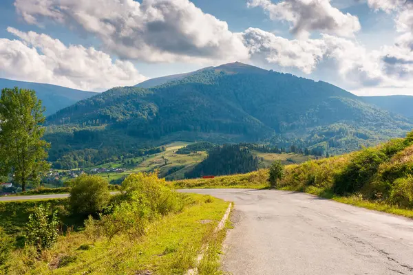 Güneşli bir akşamda dağ geçidi. Tepeden aşağı inen yol. Bulutlu gökyüzünün altında Temnatyk Tepesi 'nin önündeki Volovetler Vadisi' nin manzarası