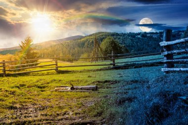 Sonbaharda dağlık kırsal alan. Gündüz ve gece zaman kavramını değiştirir. Yamaçtaki çimenli çayırdan geçen patikanın yanındaki ahşap çit. Dağlarda köknar ormanı, güneş ve ay manzarası.