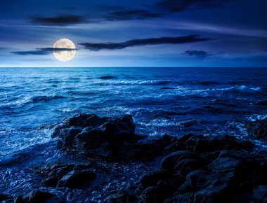 Geceleri kayalar ve kayalar olan deniz kıyıları. Deniz kıyısında sakin bir yaz tatili geçmişi. Dolunay ışığında deniz kenarında dinlenmek ve rahatlamak için harika bir sahne.