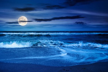Geceleri dramatik plaj arka planı. manzaralı ve bulutlu gökyüzü. Güzel deniz manzarası. Dalgalar dolunay ışığında altın kuma köpük getirir.