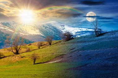 Bahar ekinoksunda dağlık kırsal alan. Gündüz ve gece değişiyor. Bir tepenin yamacındaki çimen tarlası. Uzakta karlı tepeli dağ sırtı Alacakaranlıkta güneş ve ay ile
