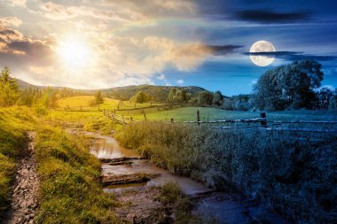 Sonbaharda dağlık kırsal alan. Gündüz ve gece zaman kavramını değiştirir. Yamaçtaki çimenli çayırdan geçen patikanın yanındaki ahşap çit. Dağlarda köknar ormanı, güneş ve ay manzarası.