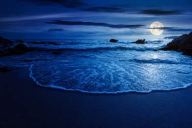 Sakin deniz manzarası. Geceleri kumlu sahilde dalgalanan kayalar. Dolunay ışığında manzaralı deniz manzarası. Rahatla ve yaz tatilinde kıyı konseptini düşün.