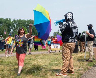 HUDSON, WI, USA - JUNE 17, 2023: Unidentified masked Anti LGBTQ+ protestors and festival attendees at Hudson Pride celebration. clipart