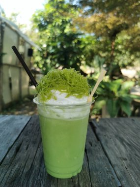 Kafe bahçesindeki ahşap masada krema ve Thai tatlısı ile kibrit yeşil çay buzlu frappe. Bulanık yeşil yapraklı tatlı bir içecek..