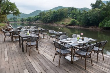 Outdoor restaurant table and chairs by kwai river with peaceful atmosphere in Kanchanaburi, Thailand.