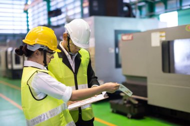 Factory auditor or inspector with hard hat check mock up blueprint at CNC milling automation robot or microchip semiconductor machine. Quality assurance for manufacturing industry.