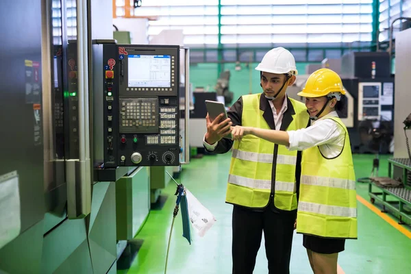Factory audit technician with hard hat using tablet at CNC milling automation robot or microchip semiconductor machine. Quality assurance for manufacturing industry.
