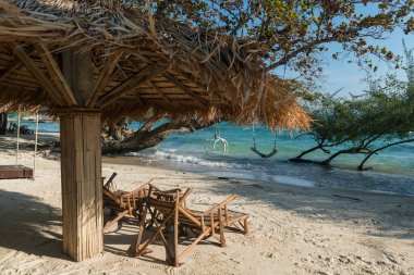 Tahta güneşlikler ya da güverte sandalyeleri saman şemsiyesinin altında mavi deniz, Ko Man Klang, Rayong, Tayland. Siyam 'daki tropikal bir ülkede ünlü seyahat ve yaz tatili.