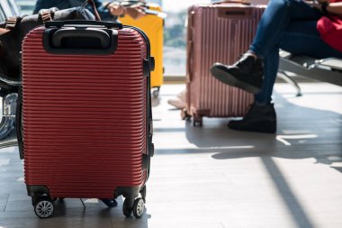 suitcase or carry-on luggage with blurred passengers sit on waiting departure seat in airport terminal. Tourist holiday maker or vacation concept.