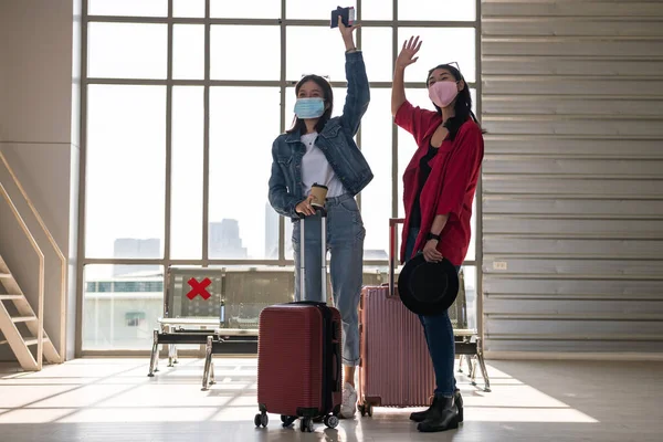 Young 2 Asian women wave hands to say hi their friends at departure airport terminal. Ready for holiday vacation by aircraft transportation.