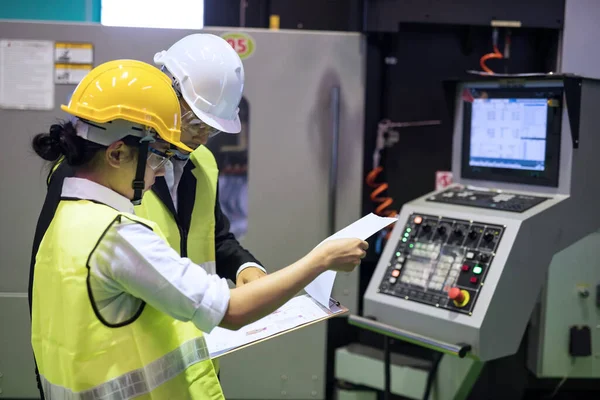 Factory auditor or inspector with hard hat check mock up blueprint at CNC milling automation robot or microchip semiconductor machine. Quality assurance for manufacturing industry. Focus at paper.