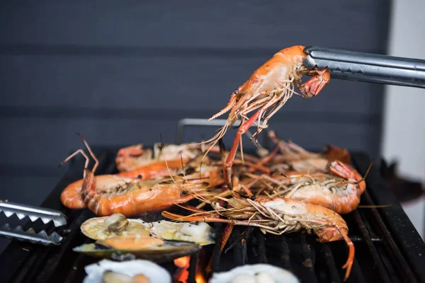 Izgara tavadan ızgara deniz karidesi tutan yemek maşaları. Akşamki aile partisi için deniz ürünleri barbeküsü ya da bbq.