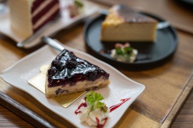 Kahve ve restorandaki ahşap masada kırmızı kadife ve peynirli kek ile yaban mersinli kek. Tatlı tatlı