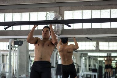 Güçlü atletik Asyalı genç adam spor salonunda kas yapmak için aynanın önüne geçiyor. Vücut geliştirme ve sağlıklı yaşam tarzı.
