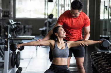Salakların kol pozisyonu için spor salonunda Asyalı güzel bir kadına vücut egzersizi yapan kişisel antrenör portresi. Mutlu Asyalı çift vücut geliştirme ve sağlıklı yaşam için çalışıyor..