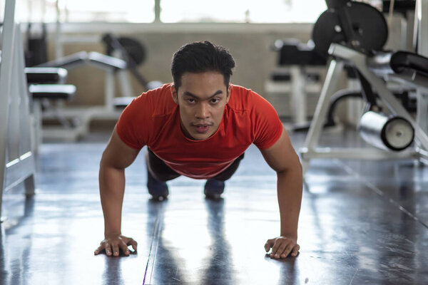 Muscular Asian young athlete man pushs up training on floor at gym. Bodybuilding exercise for shoulders, chest, biceps, triceps and forearms. Push-up and press-up.