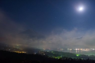 Mt ile köy aydınlansın. Fuji ve Yamanaka Gölü. Fuji Panoramadai 'nin gece görüş açısı. Yıldızlar ve ay, Yamanashi, Japonya. Ünlü seyahat yeri ve tatilci simgesi. Evin önüne odaklan.