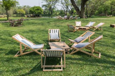 Baharda açık kafe ve restoranın bahçesindeki yeşil çimlerin üzerinde güneşli yataklar veya yatak sandalyeleri ve ahşap masa..