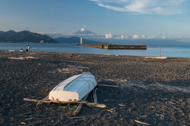 Mavi gökyüzü, Shimizu, Shizuoka Japonya 'ya karşı Fuji Dağı' nda deniz feneriyle siyah kayalıklarda bir tekne. Güzel manzaralı balıkçı ve yelkenli teknesi için ünlü bir seyahat yeri..