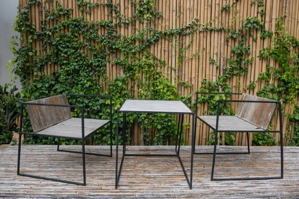 Wooden table and chairs on bamboo floor and wall with ivy climbing trees of coffee cafe patio.