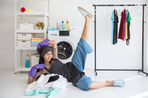 Portrait of Asian naughty young woman or wife stretching leg or yoga meditation during waiting laundry cloth in machine. Routine weekend activity to hygiene dress.