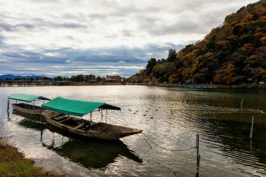 Togetsukyo köprüsü ile Katsura nehri üzerinde ahşap gezi teknesi ve sonbaharda Arashiyama, Kyoto, Japonya 'da bulutların içinden ışık huzmeleri. Kansai 'de sonbahar yeşilliklerini görmek için ünlü bir yer..