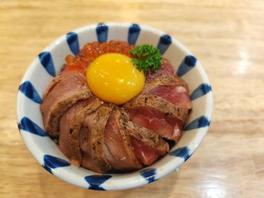 Bir kase Japon pirinci, orta pişmiş wagyu don bifteği ve yumurta sarısı ile ahşap masada..
