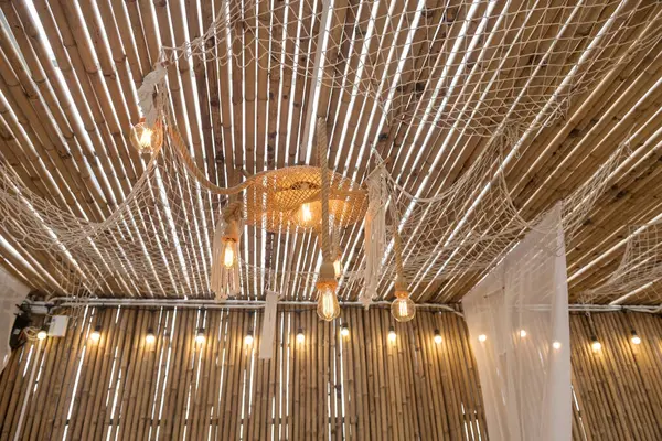 Hanging light bulbs by brown rope on bamboo ceiling in cafe and restaurant. Modern interior decoration.