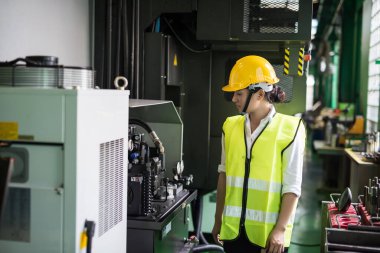 Kadın işçi, elektronik makine ve çelik ekipmanları kontrol etmek için fabrikaya gidiyor. Asyalı işçiler, güvenlik hazırlığı ve kalite kontrolü için donanımı denetliyor