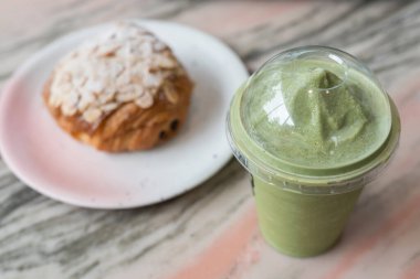 Kahve ve restoranın mermer masasında bulanık kruvasanla Macha yeşil çay frappuccino. Tatlı tatlı