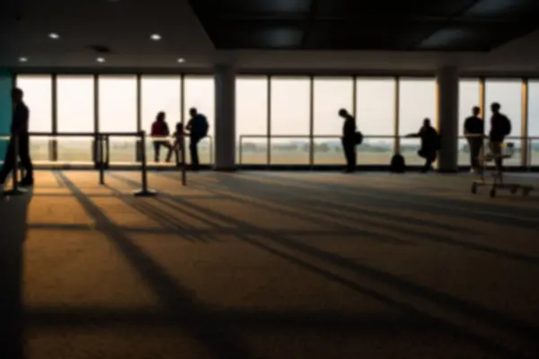 Blur image of silhouette tourist people at departure terminal gate by window wait for depart during sunrise with light shade. Holiday maker or business trip by airplane.