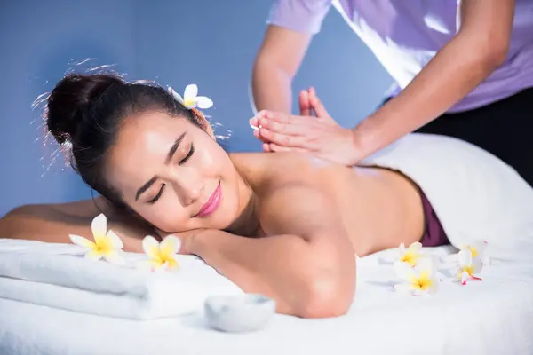 Thai oil back and spiral massage to young Asian beauty woman with white Plumeria on bed in spa salon. Body care treatment by masseuse. Alternative medical health care industry