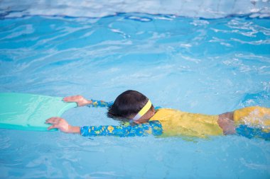 Küçük çocuk yüzen tahtada yüzme pratiği yapıyor. Genç yüzücüler için yüzme dersi. Anaokulu çocuğu yüzme havuzunda yüzmeyi öğreniyor. Küçük sporcu çocuk su altında nefes almaya çalışıyor..