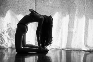 Asyalı bir kadının arka portresi göğüslerini tutuyor ve ahşap zemine doğru eğiliyor pencere kenarında açık renk tonuyla. Siyah beyaz işlemleri olan seksi kız..