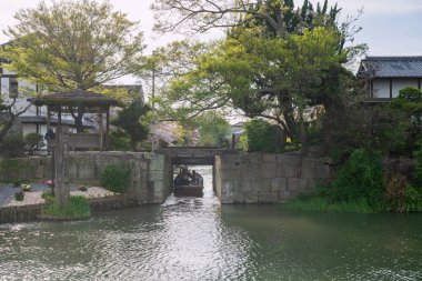 Yanagawa, Japonya - 4 Nisan 2024: Teknedeki turistler, Donkobune 'den ilkbaharda Sakura çiçeğiyle Şato Su Kapısı tüneline. Nehir boyunca gezmek ve gezmek için ünlü bir seyahat yeri.