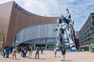 Turistler, Mitsui Alışveriş Parkı LaLaport 'un önündeki mavi gökyüzüne karşı Gundam gerçek boyutundaki RX 93ff robot heykelini ziyaret ediyor..