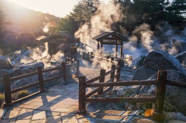 Jigoku Dağı Dağı ve gün batımında Shimabara şehri Nagasaki, Kyushu, Japonya 'dan yoğun sülfür gazı buharı ile sıcak kaynaklar. Sıcak su, gazlar ve buhar volkanik kaynak alanından fışkırıyor..