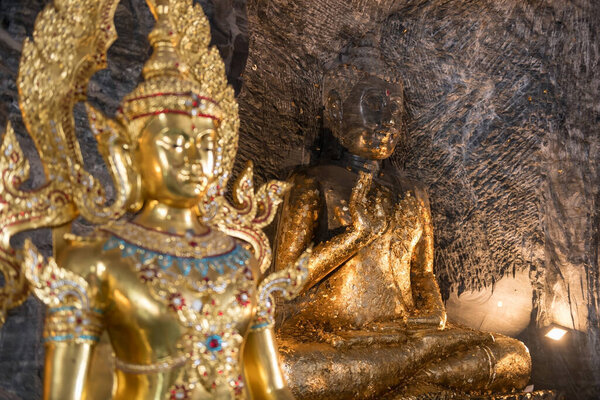 Ancient stone Buddha statue and golden god inside mountian cave tunnel of Wat Khao Tham Thiam, Suphan buri, Thailand. Famous travel destination in Siam.