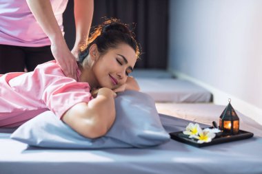 Tayland omuz masajı. Masöz, mum ve kaplıca salonundaki Plumeria çiçeği. Gülümseyen Asyalı güzel bir kadının portresi tedavi için rahatlıyor. Alternatif sağlık sektörü
