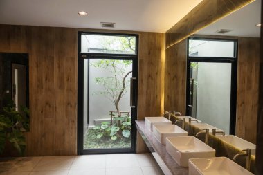 İç dizaynında birçok lavabo, tuvalet ve kapı var. Banyodaki ağacın dışından geçiyor. Modern bir binada şık bir tuvalet..