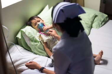 Hemşire hasta çocuk solunum terapisine oksijen maskesi veriyor. RSV 'si olan hasta küçük bir çocuk, Solunum Senkronizasyon Virüsü, sorun. Hastane yatağında nebulizörden nefes alıyor..