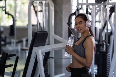 Jimnastik salonunda kulaklık takan güzel, Asyalı, formda genç bir kadın. Gülümseyen sağlıklı kız spor yaptıktan sonra ara veriyor. Vücut geliştirme ve sağlıklı yaşam tarzı konsepti